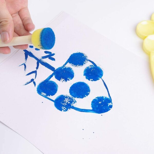 A child happily dab painting on paper with a yellow sponge dabber.